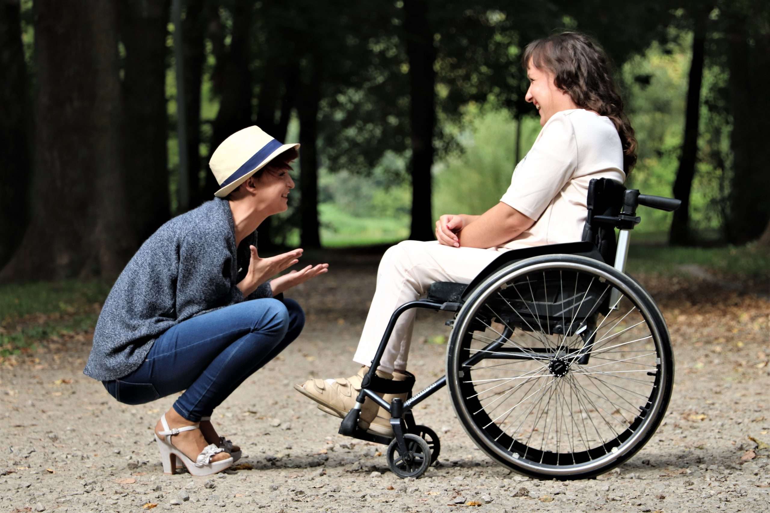Frau kniet vor Frau im Rollstuhl und beide lachen